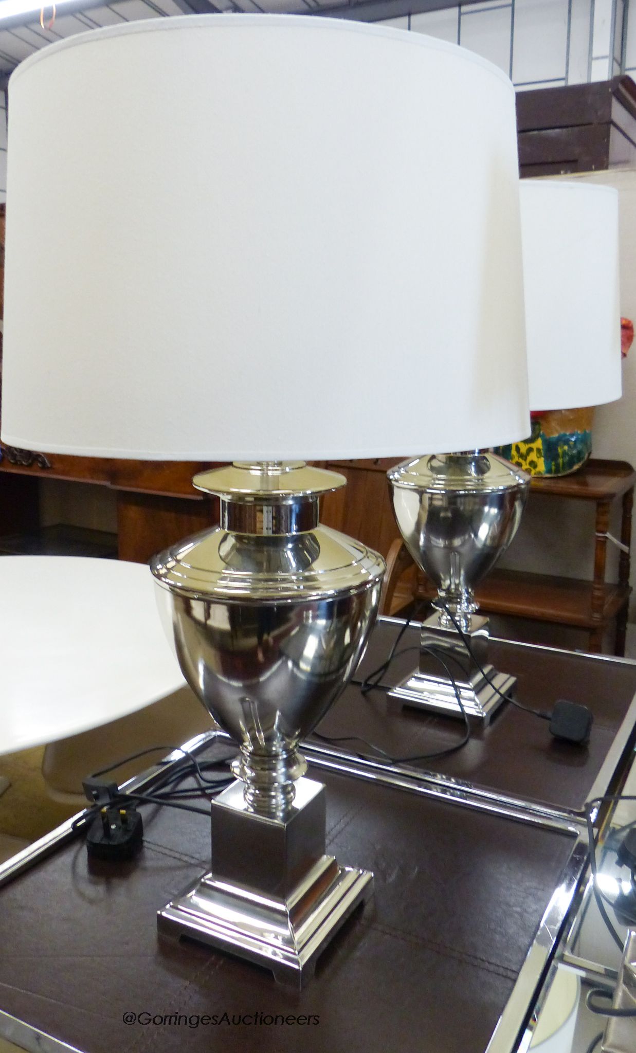 A pair of chrome urn form table lamps with cream shades by Andrew Martin